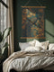 A wall tapestry featuring a detailed teal peacock with golden accents and intricate plumage, surrounded by ornate golden flowers and foliage on an emerald green background, mounted between wooden dowels with twine.